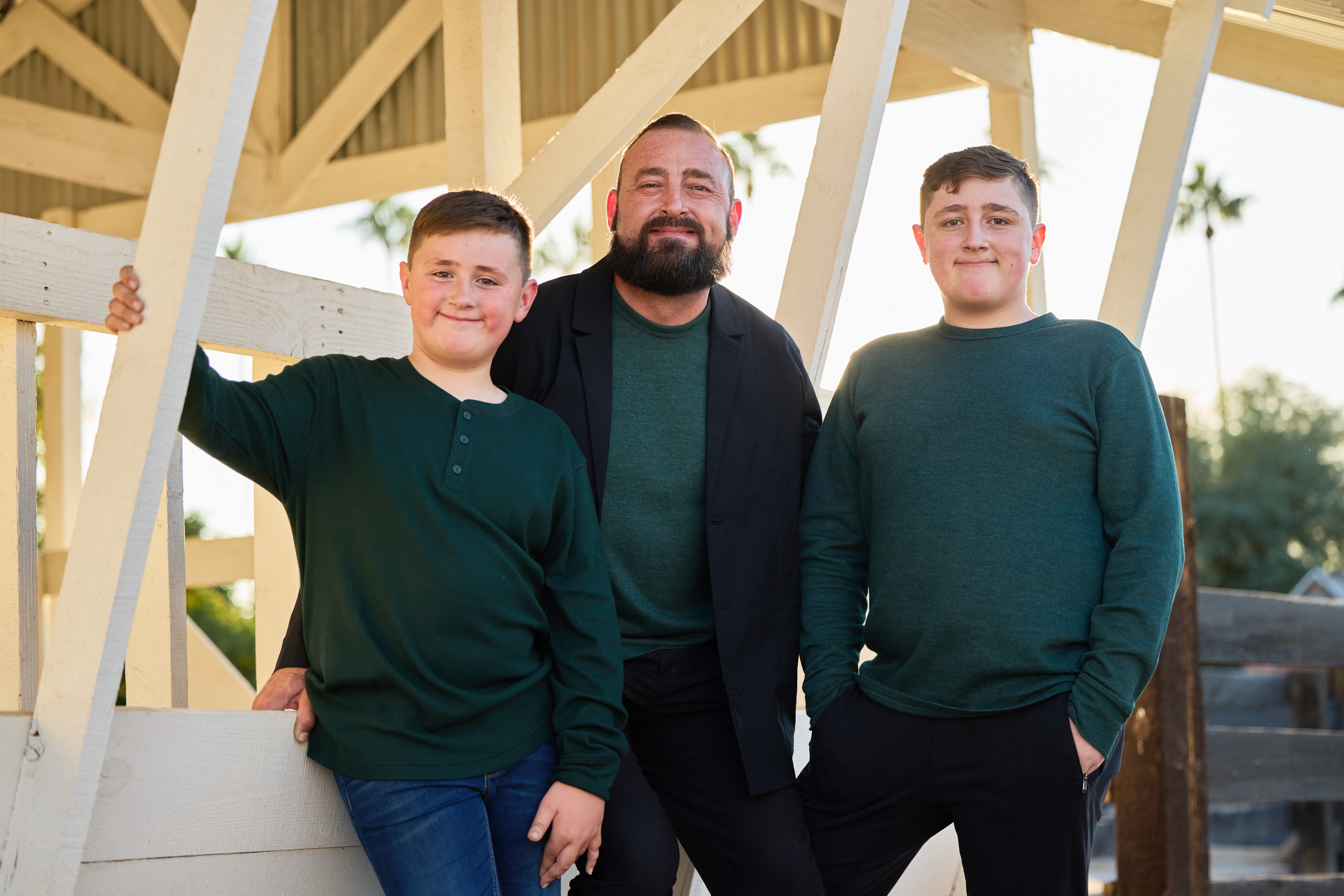 Dad with his two sons framed by white barn beams and golden light.