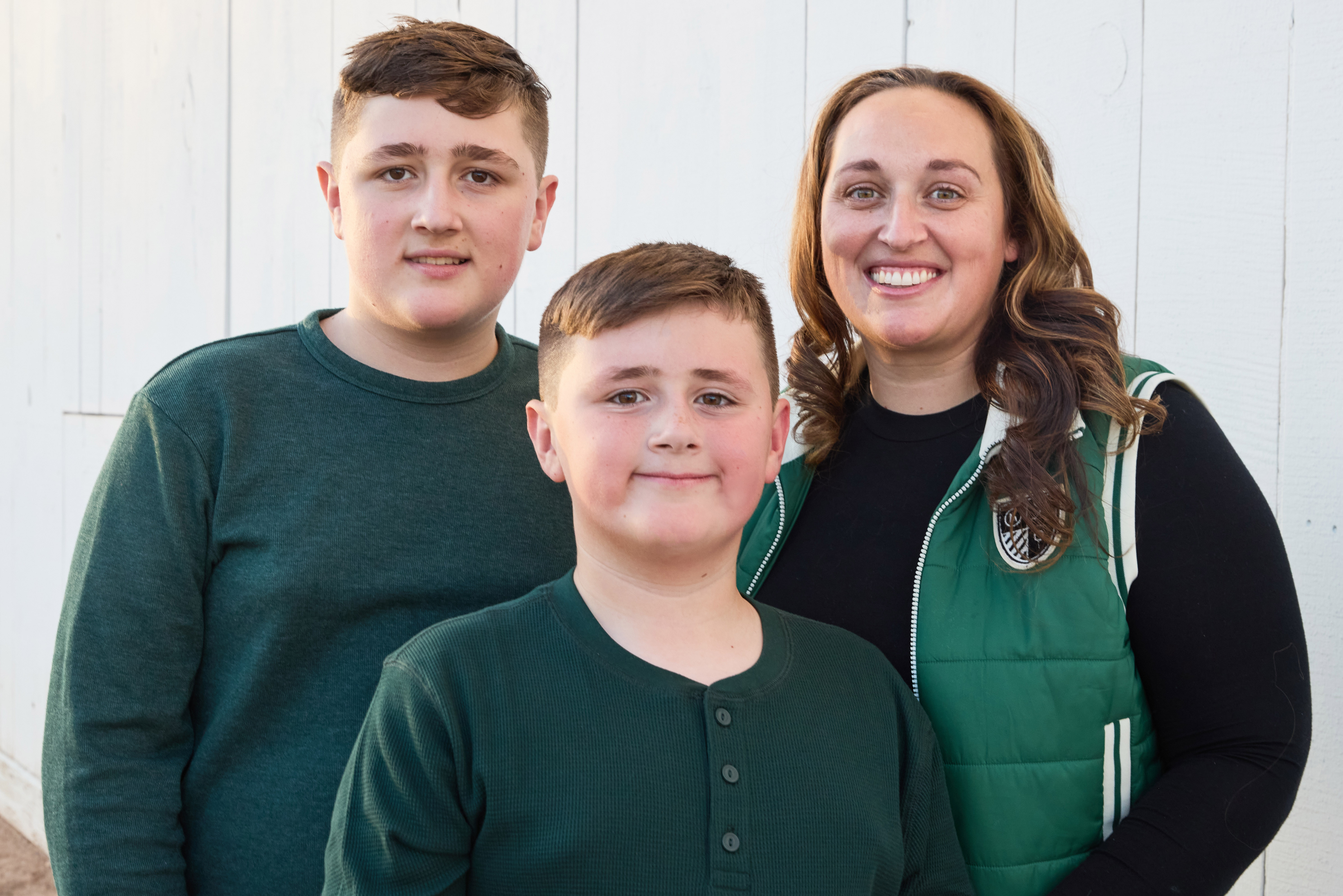 Mom with her two sons smiling against the white barn wall.