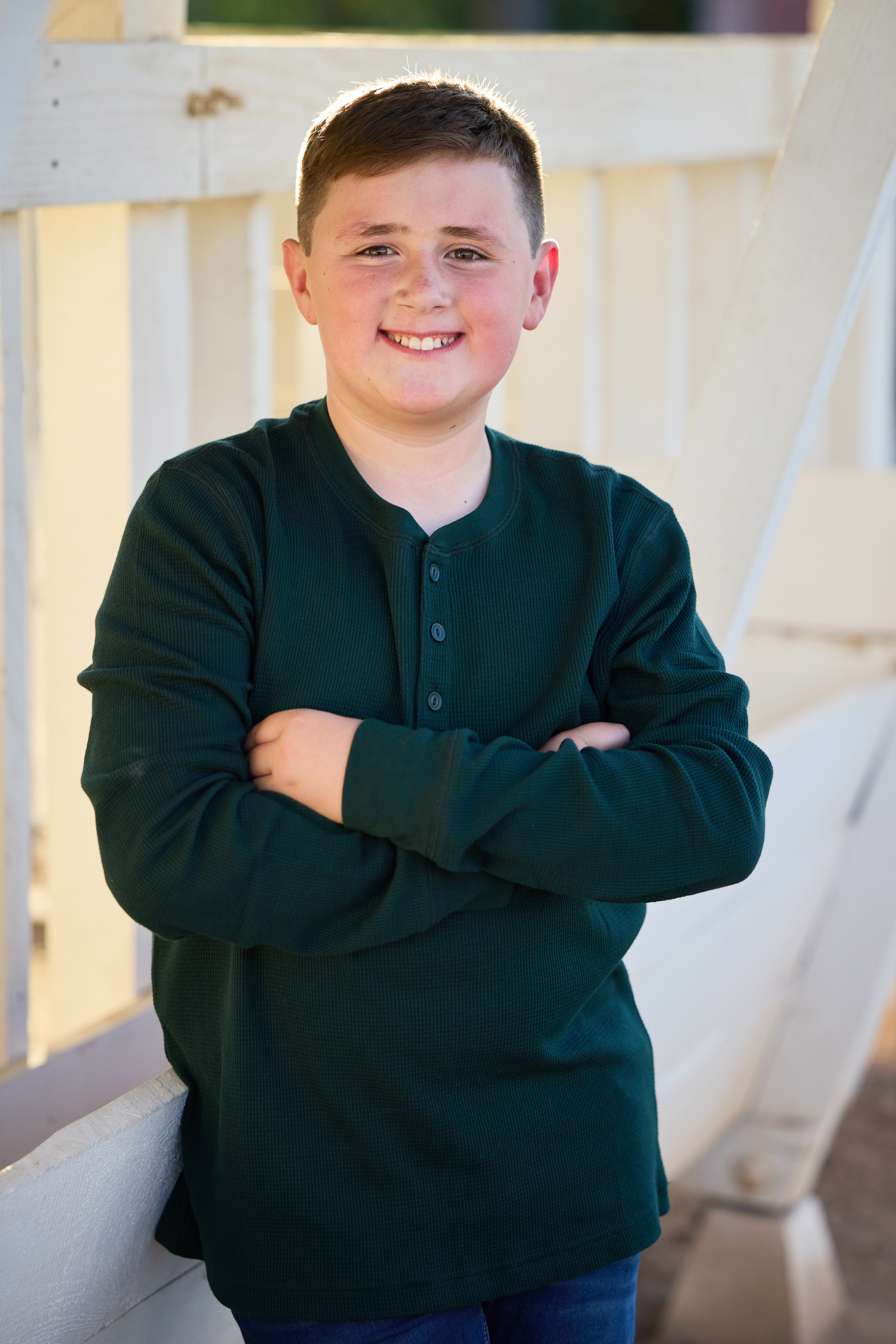 Younger son smiling with arms crossed beside the barn railing.